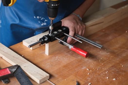 Woodworking entrepreneurs are using a drill through the wood holes to assemble and build wooden tables for customers.