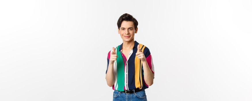 Confident handsome man encourage you, pointing fingers at camera and smiling, being supportive, standing over white background.