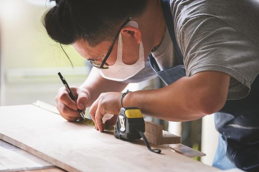 A carpenter measures the planks to assemble the parts and build a wooden table for the customer