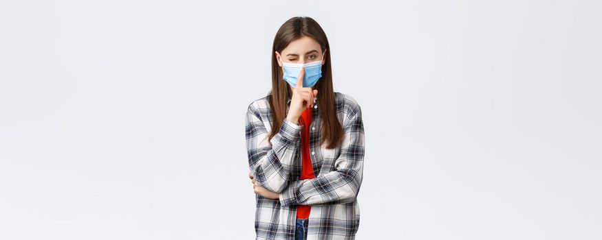 Coronavirus outbreak, leisure on quarantine, social distancing and emotions concept. Attractive young woman in checked casual shirt and medical mask ask keep secret, press finger to lips shush.