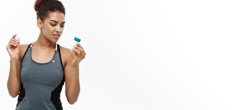 Healthy and healthcare concept - portrait of beautiful sporty African American holding bottle of supplementary bottle. Isolated on white studio background