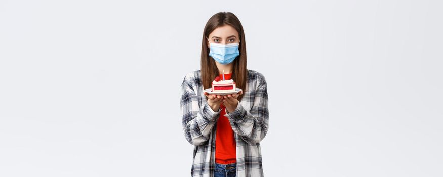 Coronavirus outbreak, lifestyle during social distancing and holidays celebration concept. Cute young woman in medical mask celebrating birthday alone during quarantine, hold b-day cake.