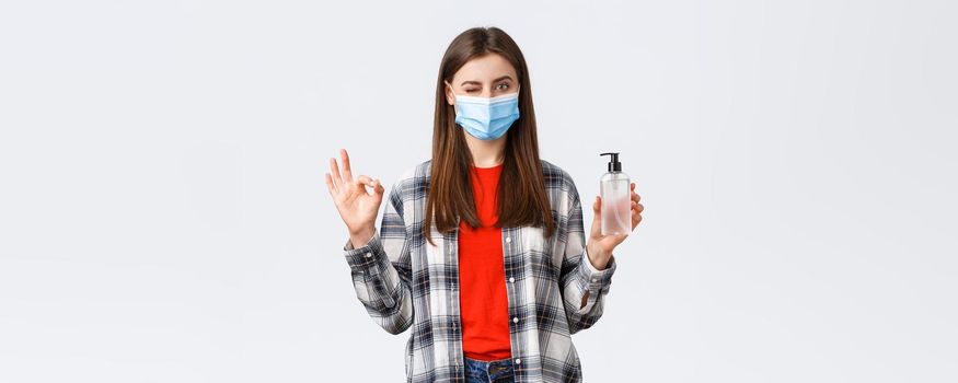 Coronavirus outbreak, leisure on quarantine, social distancing and emotions concept. No problem. Pleased cute girl in medical mask show okay sign and wink as advertise hand sanitizer.