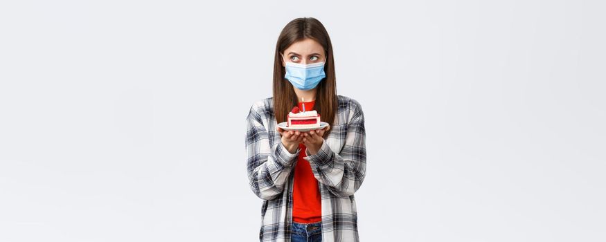 Coronavirus outbreak, lifestyle during social distancing and holidays celebration concept. Serious birthday girl in medical mask, focus on making wish, thinking as hold b-day cake with lit candle.