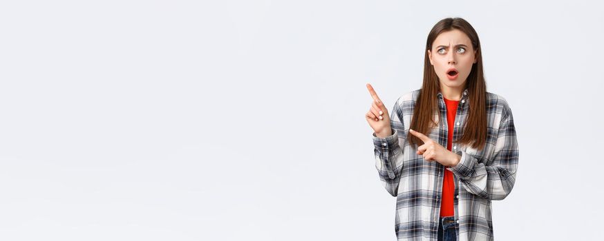 Lifestyle, different emotions, leisure activities concept. Shocked and concerned young pretty woman in checked casual shirt, pointing and looking upper left corner with displeased shook face.