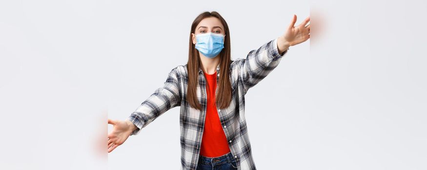 Coronavirus outbreak, leisure on quarantine, social distancing and emotions concept. Cute young woman in medical mask on self-isolation with family, spread hands sideways, dreaming of hugging you.