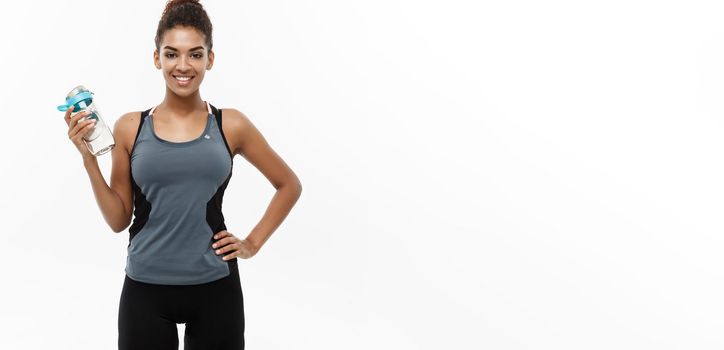 Healthy and Fitness concept - beautiful African American girl in sport clothes holding water bottle after workout. Isolated on white studio background.