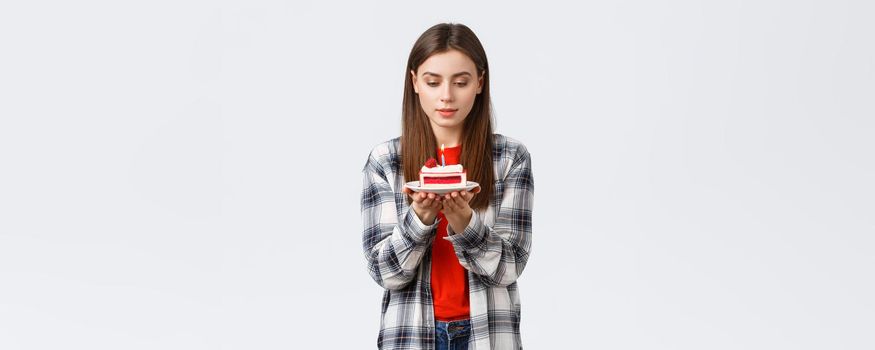 People lifestyle, holidays and celebration, emotions concept. Dreamy attractive birthday girl, woman celebrating b-day, making wish look at lit candle on cake, white background.