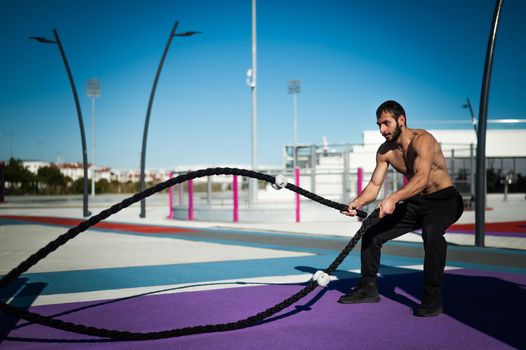 Shirtless man doing exercises with ropes outdoors