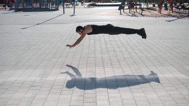 A man in black sportswear jumps doing push-ups in the park