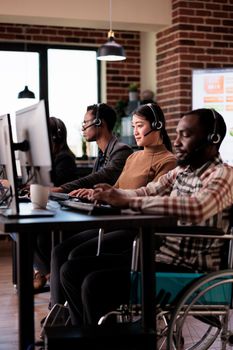 Paralyzed wheelchair user working at call center helpline reception with physical impairment. Male operator living with disability and chronic pain, helping clients at customer service support.