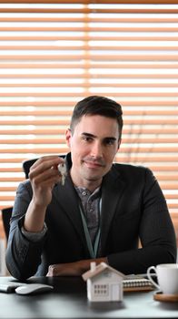 Portrait estate agent holding house key and smiling to camera. Insurance or loan real estate concept.