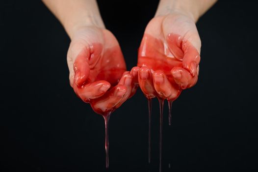 Women's hands in a viscous red liquid similar to blood