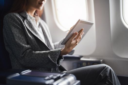 A successful asian businesswoman or female entrepreneur in formal suit in a plane sits in a business class's seat and uses a tablet computer during flight.