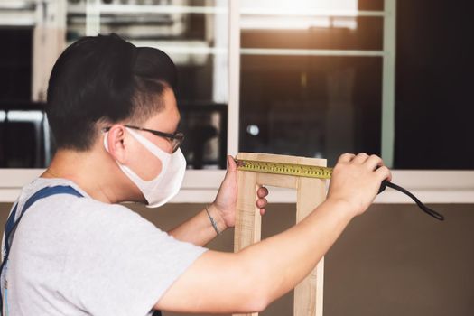 A carpenter measures the planks to assemble the parts and build a wooden table for the customer