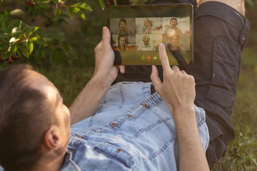 Young Man with a Tablet Computer on the Green Leaves Background outdoor