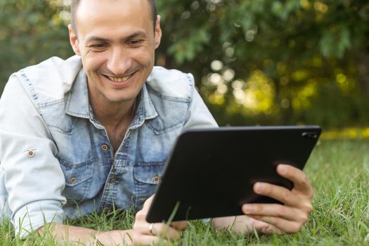 Young Man with a Tablet Computer on the Green Leaves Background outdoor