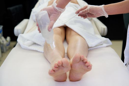 Cosmetologist preparing female patient for laser hair removal on legs