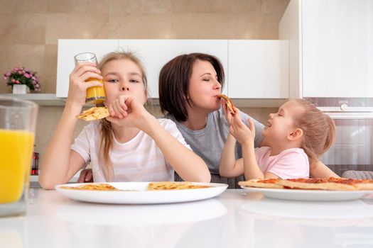 Mother and two daughters eating homemade pizza at a table in kitchen