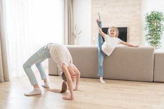 Two sisters doing yoga stretching exercises in living room at home