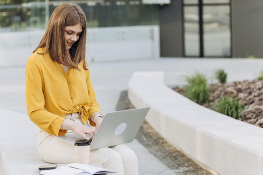 European woman with long hair student freelancer sitting outdoors in city using wireless laptop online video call conference chat talking to webcam.