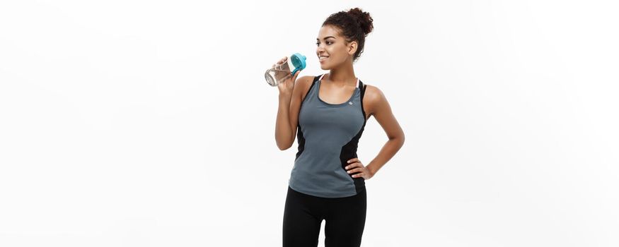 Healthy and Fitness concept - beautiful African American girl in sport clothes drinking water after workout. Isolated on white studio background.