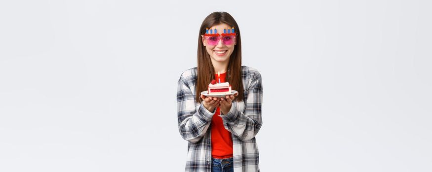 People lifestyle, holidays and celebration, emotions concept. Cheerful cute girl in glasses holding birthday cake, celebrate b-day, making wish to blow lit candle, white background.