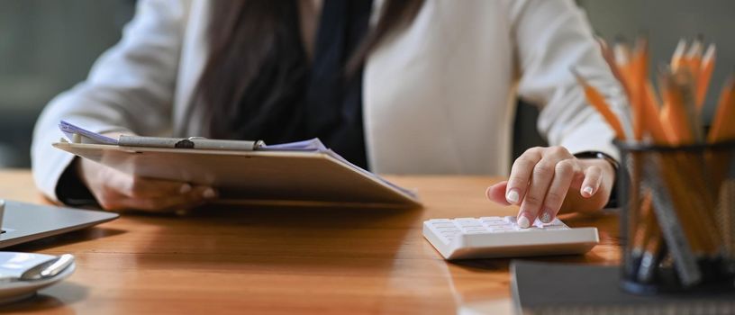 Young businesswoman holding financial documents and using calculator.