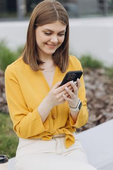Vertical portrait of business woman reading messages on cellphone. Happy businesswoman using mobile phone at remote workplace. Smiling woman browsing internet on smartphone near office.