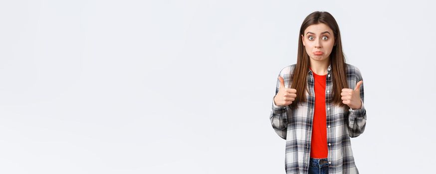 Lifestyle, different emotions, leisure activities concept. Not bad I guess. Cute girl surprised with positive result, show thumb-up and make confused expression, standing white background.