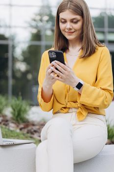 Appealing young elegant caucasian woman using social media application on smartphone text messages receive news smiling outdoor. People portraits and technology concept.