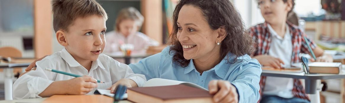 Happy kind teacher is helping a boy in elementary school lessons.