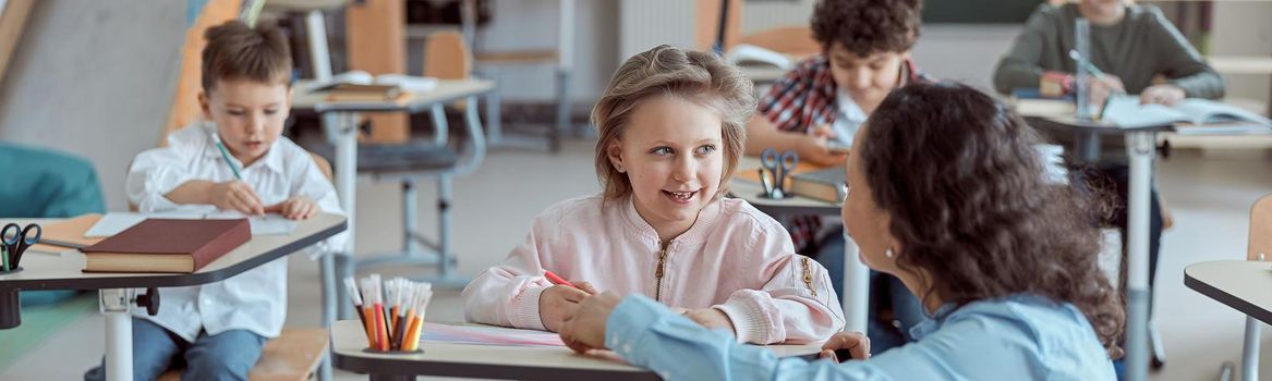 Happy kind teacher is helping kids in elementary school lessons.