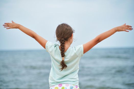 Happy child looking at the sea. Kid girl having fun at the beach. Summer vacation and active lifestyle concept