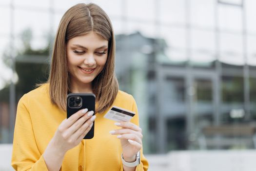 Female hand typing bank card number into a smartphone. Caucasian woman holding credit card using a digital mobile device and buying online, internet shopping.