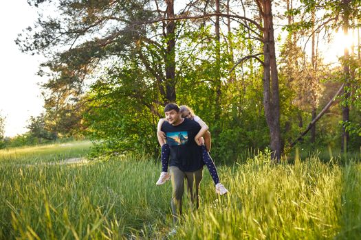 Father giving piggyback ride to small daughter on a walk in summer forest.