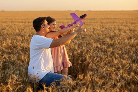 Cute girl and her father playing with toy airplane against sky in wheat field