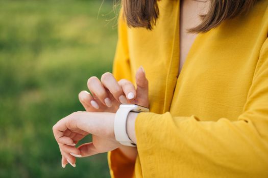 Young woman browsing notificatins on modern smart wristwatches connected to internet. Female using touchscreen on gadget. Smart watch on woman's hand outdoor. Girl using smartwatches.