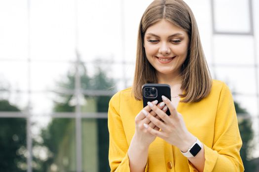 People portraits and technology concept. Appealing young elegant caucasian woman using social media application on smartphone text messages receive news smiling outdoor.