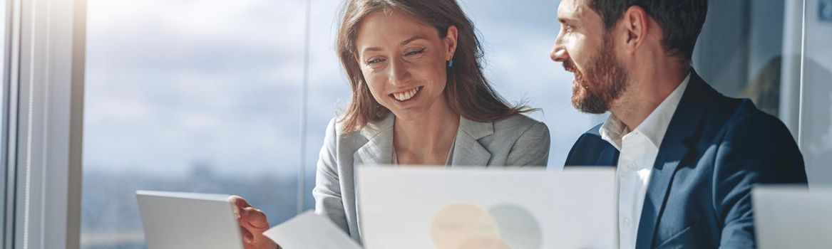 Two business people in office explaining statistics data to each other looking at documents