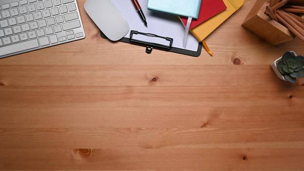 Top view wireless keyboard and office supplies on wooden table.