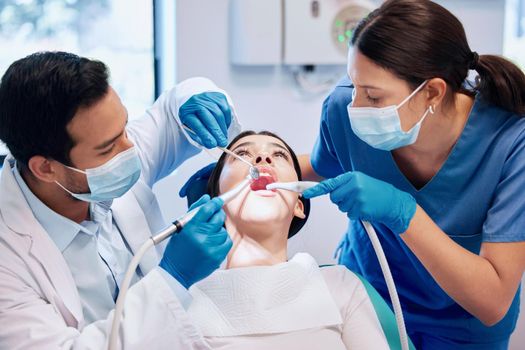 Shot of a young dentist working on a patients teeth with his assistant.