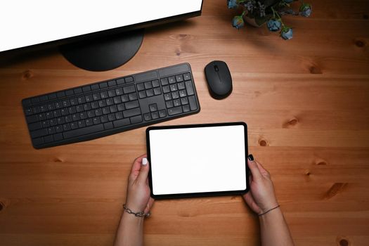 Young woman sitting in front of computer and using digital tablet.