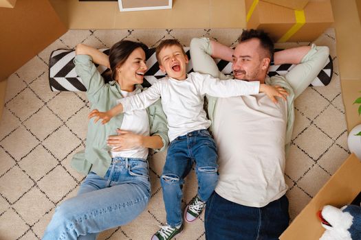 Happy family lying on the floor in new home with cordboard boxes around, close up