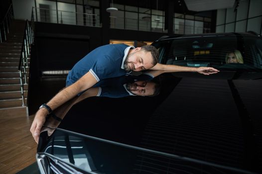 Happy caucasian man hugging the hood of his new car in a car dealership