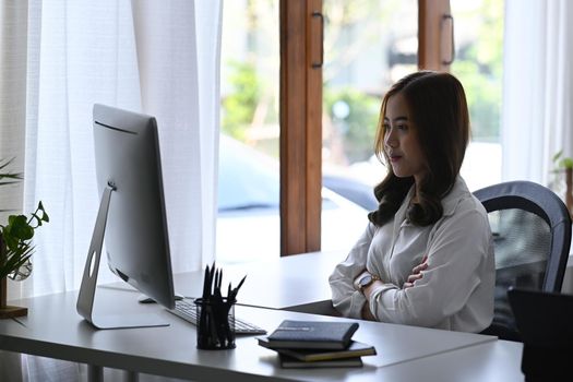 Confident businesswoman sitting at her workplace and reading email on computer.