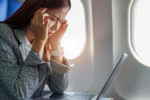 portrait of a successful Asian businesswoman or entrepreneur in a formal suit on an airplane seated in Business Class shows a thoughtful and stressed face with using laptop during the flight.