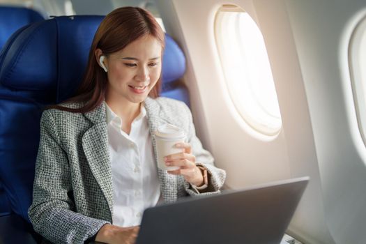 portrait of A successful asian businesswoman or female entrepreneur in formal suit in a plane sits in a business class seat and uses a computer laptop during flight.