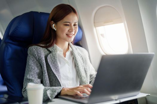 portrait of A successful asian businesswoman or female entrepreneur in formal suit in a plane sits in a business class seat and uses a computer laptop during flight.