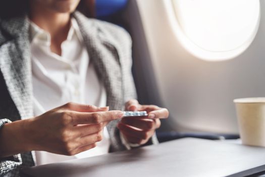 a successful Asian businesswoman or entrepreneur in a formal suit on an airplane in business class taking motion sickness pills during the flight.